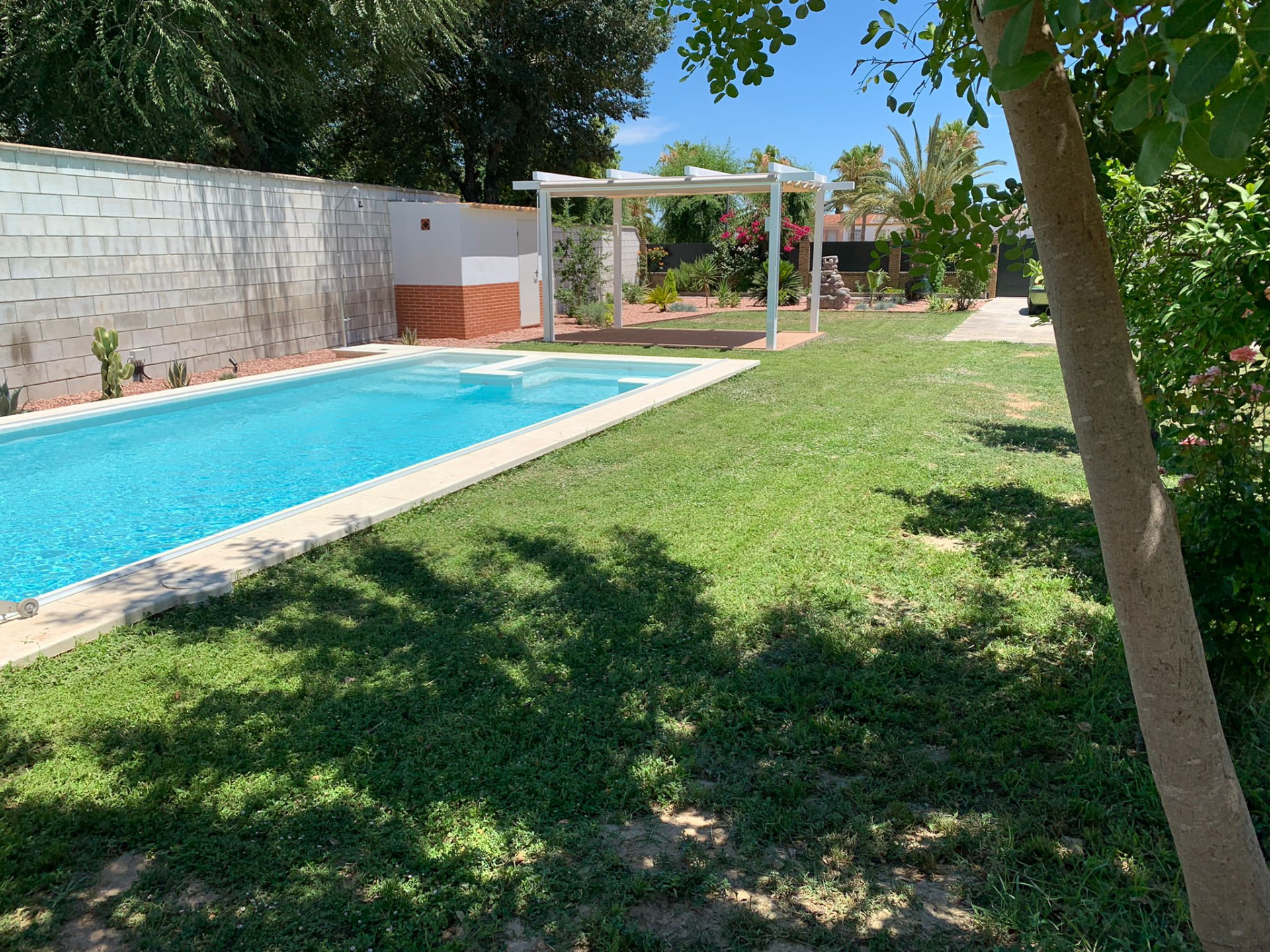 Jardín con piscina, césped y pérgola en una vivienda del Aljarafe