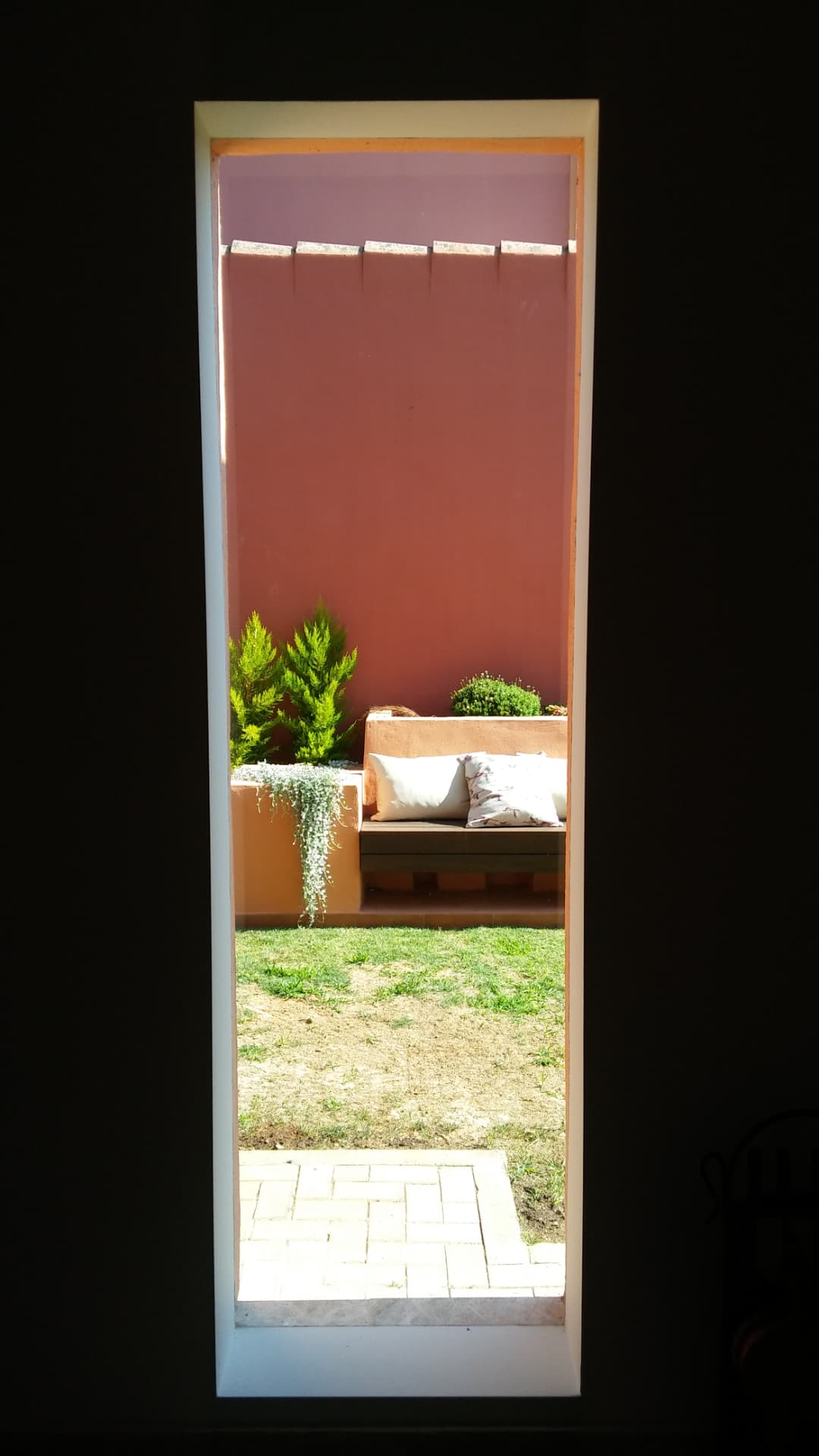 Vista del jardín con banco y jardineras desde el interior de la vivienda