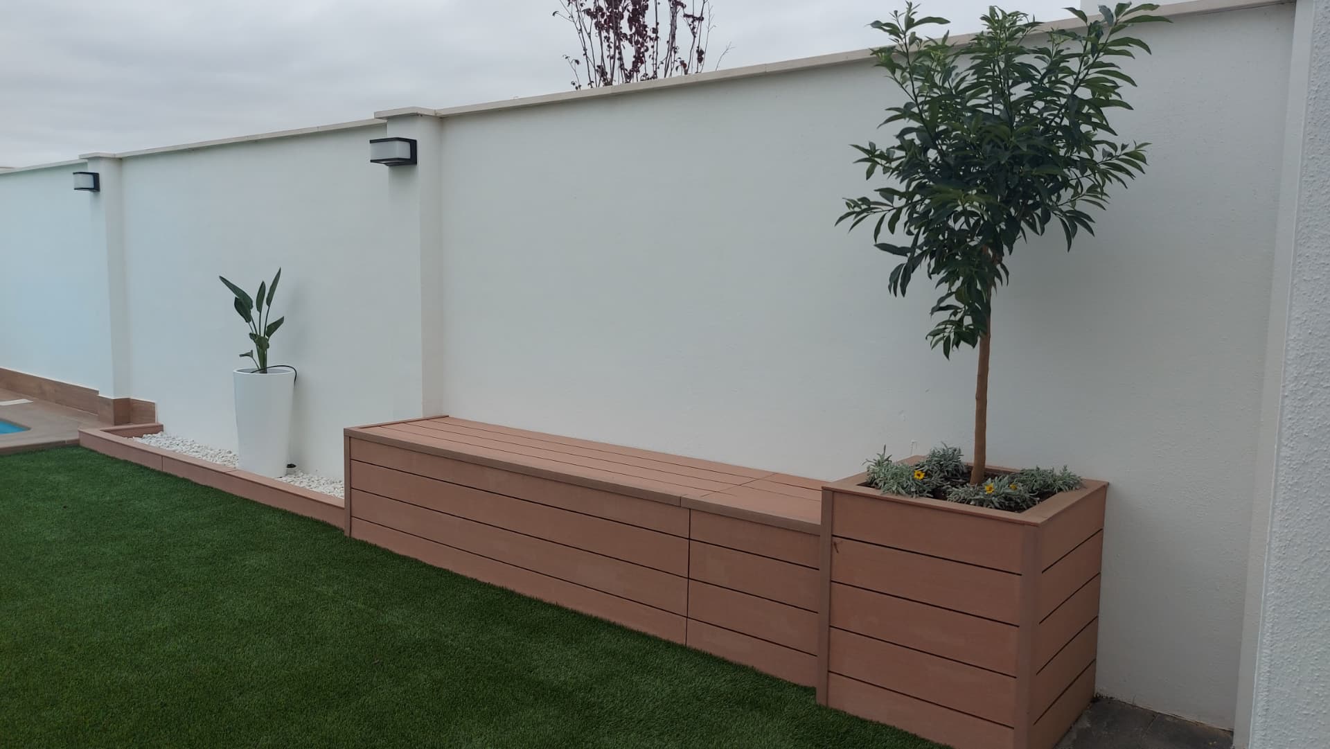 Banco corrido y jardineras de composite color terracota junto a césped y muro blanco